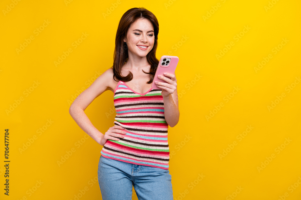 Portrait of clever positive woman with piercing wear tank look at smartphone read notification isolated on vivid yellow color background Portrait of clever positive woman with piercing wear tank look at smartphone read notification isolated on vivid yellow color background