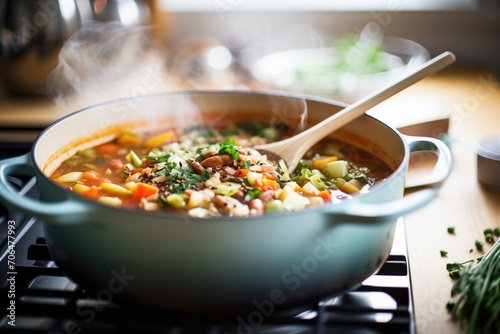 minestrone cooking in pot, wooden spoon stir photo