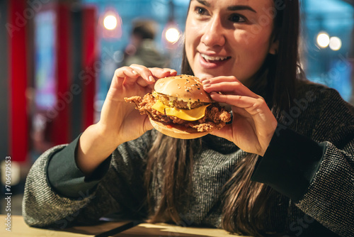An appetizing chicken burger in female hands in a fast food restaurant.