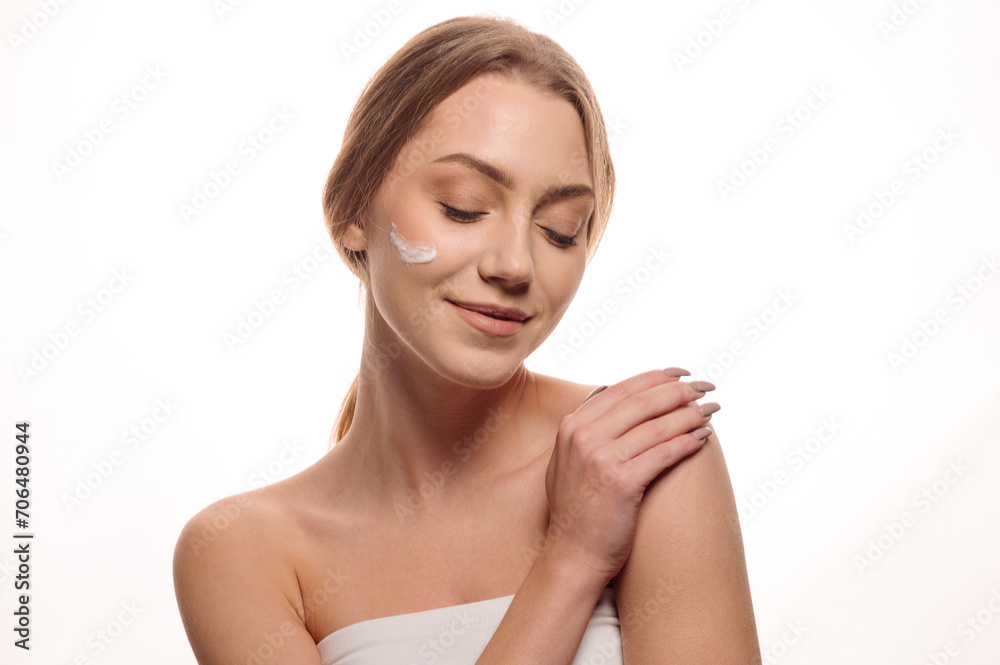 Beauty portrait of a beautiful blonde girl applying cream on her face on an isolated white background