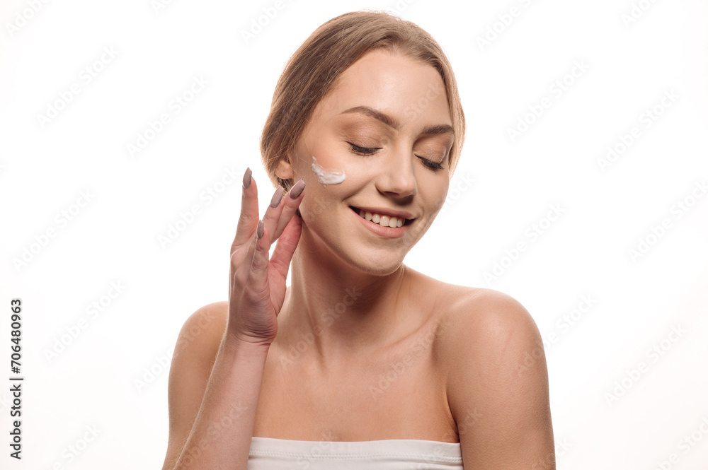 Beauty portrait of a beautiful blonde girl applying cream on her face on an isolated white background