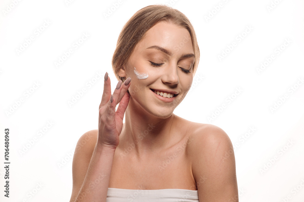 Beauty portrait of a beautiful blonde girl applying cream on her face on an isolated white background Beauty portrait of a beautiful blonde girl applying cream on her face on an isolated white background