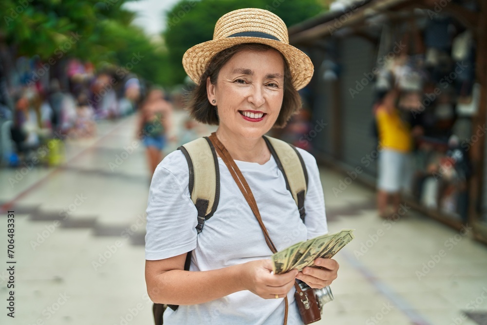 Middle age woman tourist smiling confident counting dollars at street market