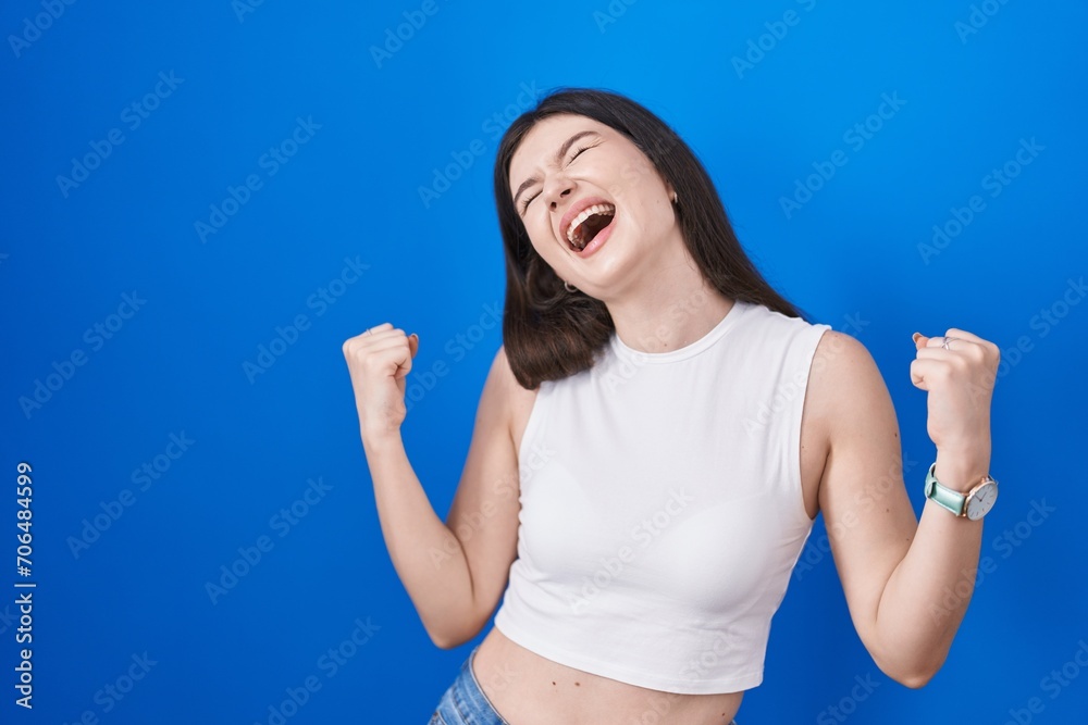 Young caucasian woman standing over blue background celebrating surprised and amazed for success with arms raised and eyes closed. winner concept. Young caucasian woman standing over blue background celebrating surprised and amazed for success with arms raised and eyes closed. winner concept.