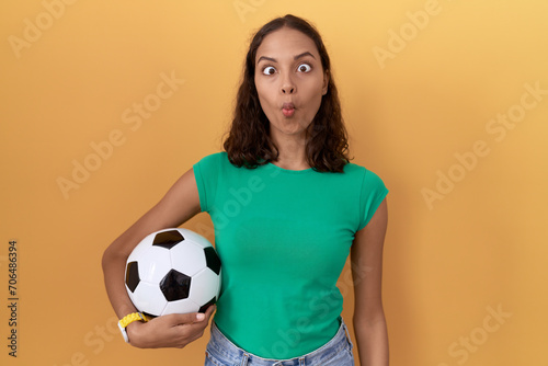 Young hispanic woman holding ball making fish face with lips, crazy and comical gesture. funny expression. © Krakenimages.com