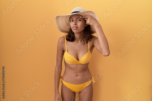 Young hispanic woman wearing bikini and summer hat pointing unhappy to pimple on forehead  ugly infection of blackhead. acne and skin problem