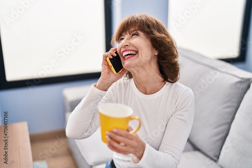 Middle age woman talking on smartphone drinking coffee at home