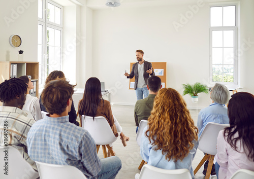 Young business man talking about work project for a group of company employees sitting back in meeting room. Diverse business people discussing company growth on a conference in office.