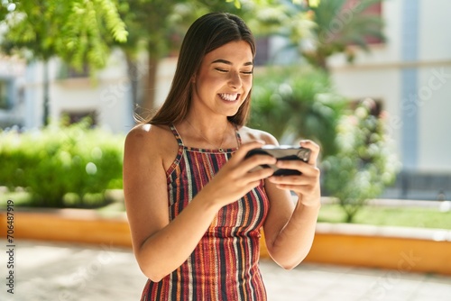 Young beautiful hispanic woman smiling confident playing video game at park photo
