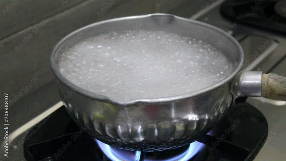Small pan or silver pot with boiling water, in the kitchen, on top of a gas stove with blue fire. Bubbles of boiling water Small pan or silver pot with boiling water, in the kitchen, on top of a gas stove with blue fire. Bubbles of boiling water