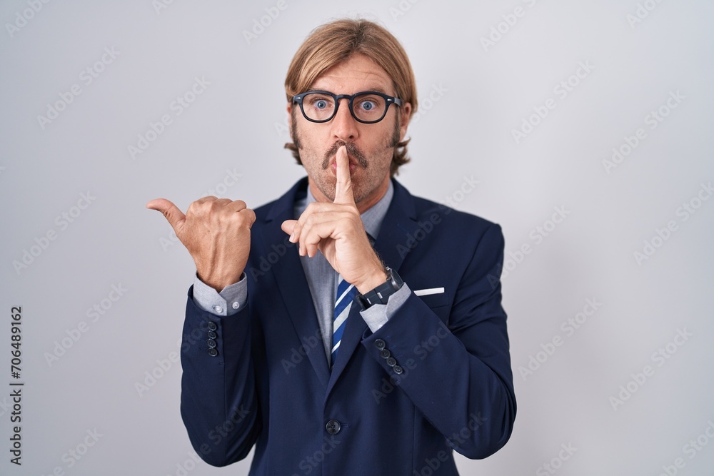 Caucasian man with mustache wearing business clothes asking to be quiet with finger on lips pointing with hand to the side. silence and secret concept. Caucasian man with mustache wearing business clothes asking to be quiet with finger on lips pointing with hand to the side. silence and secret concept.