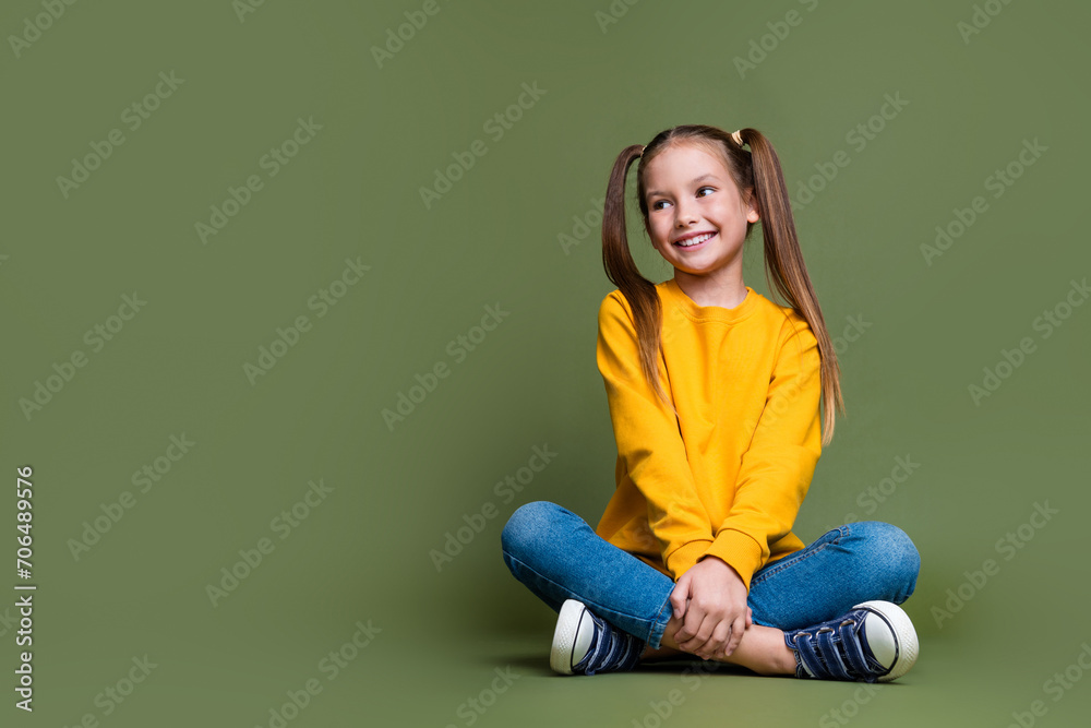 Full size photo of cute little schoolgirl with ponytails wear yellow pullover look at sale empty space isolated on khaki color background Full size photo of cute little schoolgirl with ponytails wear yellow pullover look at sale empty space isolated on khaki color background