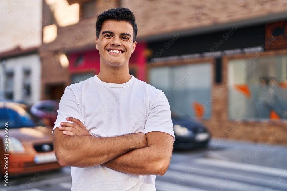 Young hispanic man standing with arms crossed gesture at street