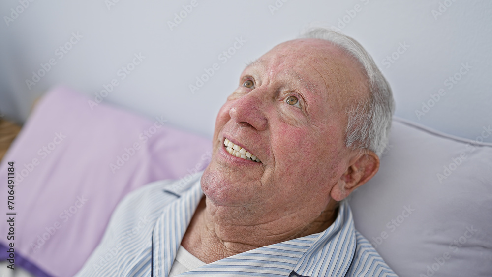 Obraz premium Confident senior man, with a heartwarming smile, enjoying a cozy morning lying in bed within the intimate atmosphere of his comfortable bedroom.