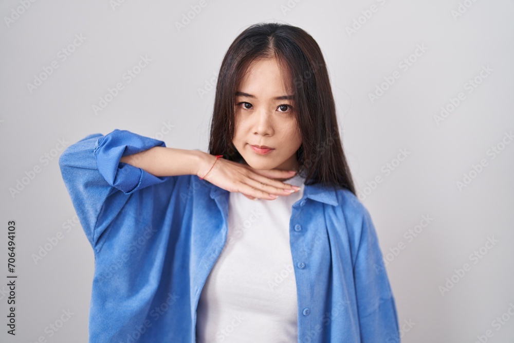 Young chinese woman standing over white background cutting throat with hand as knife, threaten aggression with furious violence Young chinese woman standing over white background cutting throat with hand as knife, threaten aggression with furious violence