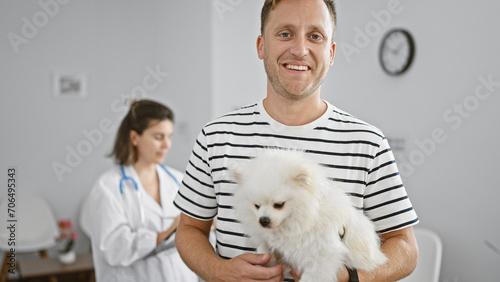 Fototapeta Naklejka Na Ścianę i Meble -  Happy young caucasian man confidently standing with his smiling dog in the vibrant, lively waiting room of a trusted veterinary clinic