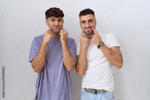 Homosexual gay couple standing over white background smiling with open mouth, fingers pointing and forcing cheerful smile