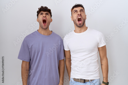 Homosexual gay couple standing over white background angry and mad screaming frustrated and furious, shouting with anger. rage and aggressive concept.