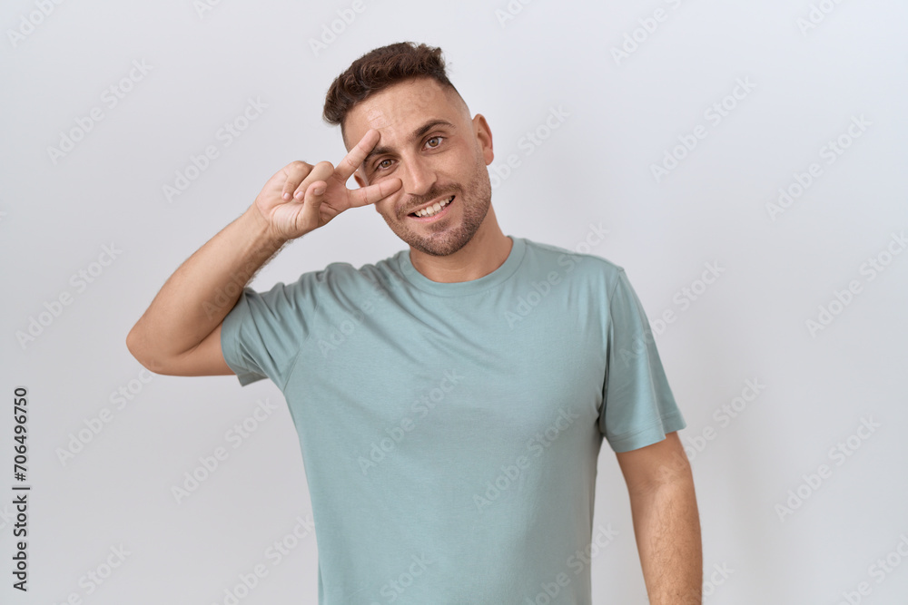 Hispanic man with beard standing over white background doing peace symbol with fingers over face, smiling cheerful showing victory Hispanic man with beard standing over white background doing peace symbol with fingers over face, smiling cheerful showing victory