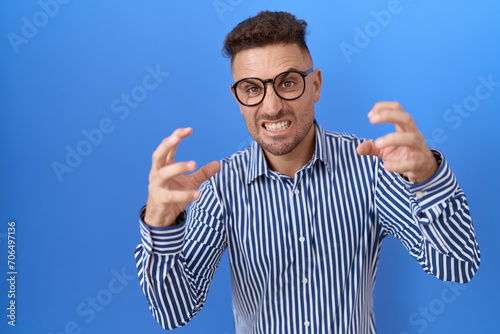 Hispanic man with beard wearing glasses shouting frustrated with rage, hands trying to strangle, yelling mad