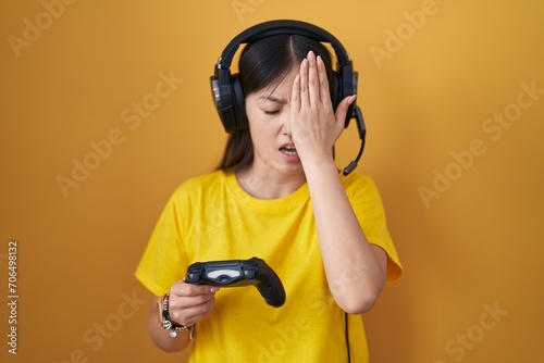 Chinese young woman playing video game holding controller yawning tired covering half face, eye and mouth with hand. face hurts in pain.
