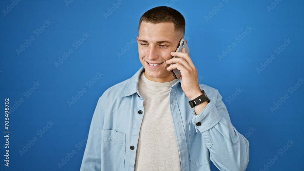 A young, handsome hispanic man smiling while talking on a smartphone against a blue outdoor wall, expressing connectivity and ease. A young, handsome hispanic man smiling while talking on a smartphone against a blue outdoor wall, expressing connectivity and ease.