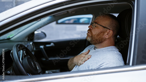 Handsome middle-aged, bearded caucasian man, feeling heart attack pain while driving car on urban city street, stressed and anxious from traffic frustration