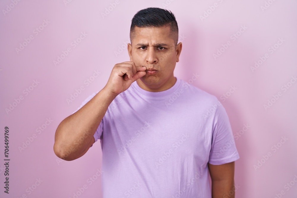 Young hispanic man standing over pink background mouth and lips shut as zip with fingers. secret and silent, taboo talking