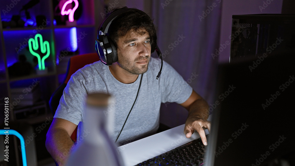 A focused man with headphones uses a laptop in a neon-lit gaming room at night. A focused man with headphones uses a laptop in a neon-lit gaming room at night.