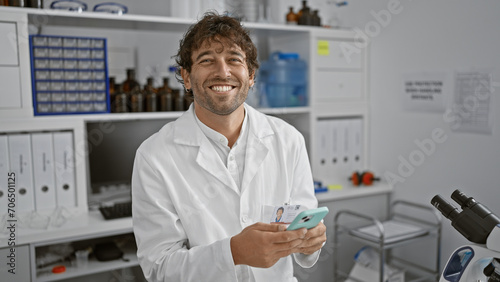 A smiling handsome hispanic man with a beard using a smartphone in a laboratory setting  representing a healthcare professional at work.