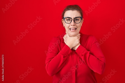 Young hispanic woman with red hair standing over red background shouting and suffocate because painful strangle. health problem. asphyxiate and suicide concept.