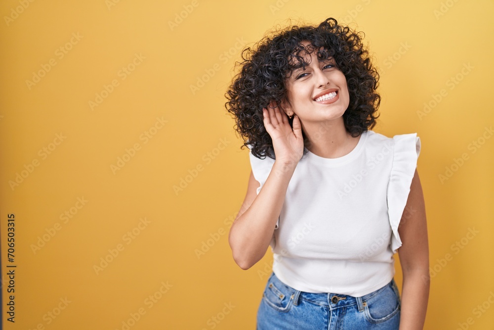 Young middle east woman standing over yellow background smiling with hand over ear listening an hearing to rumor or gossip. deafness concept. Young middle east woman standing over yellow background smiling with hand over ear listening an hearing to rumor or gossip. deafness concept.