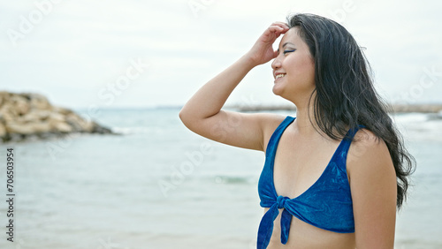 Young chinese woman tourist wearing bikini combing hair smiling at the beach