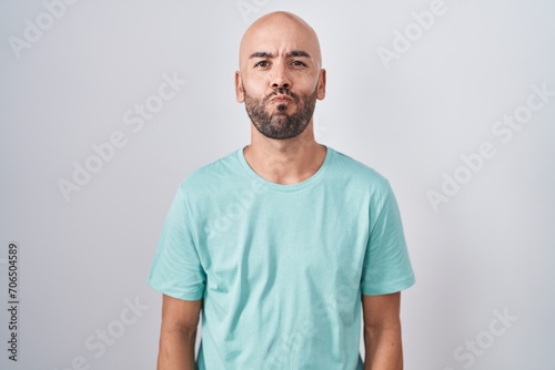 Middle age bald man standing over white background puffing cheeks with funny face. mouth inflated with air, crazy expression.