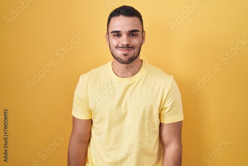 Young hispanic man standing over yellow background puffing cheeks with funny face. mouth inflated with air, crazy expression. photo
