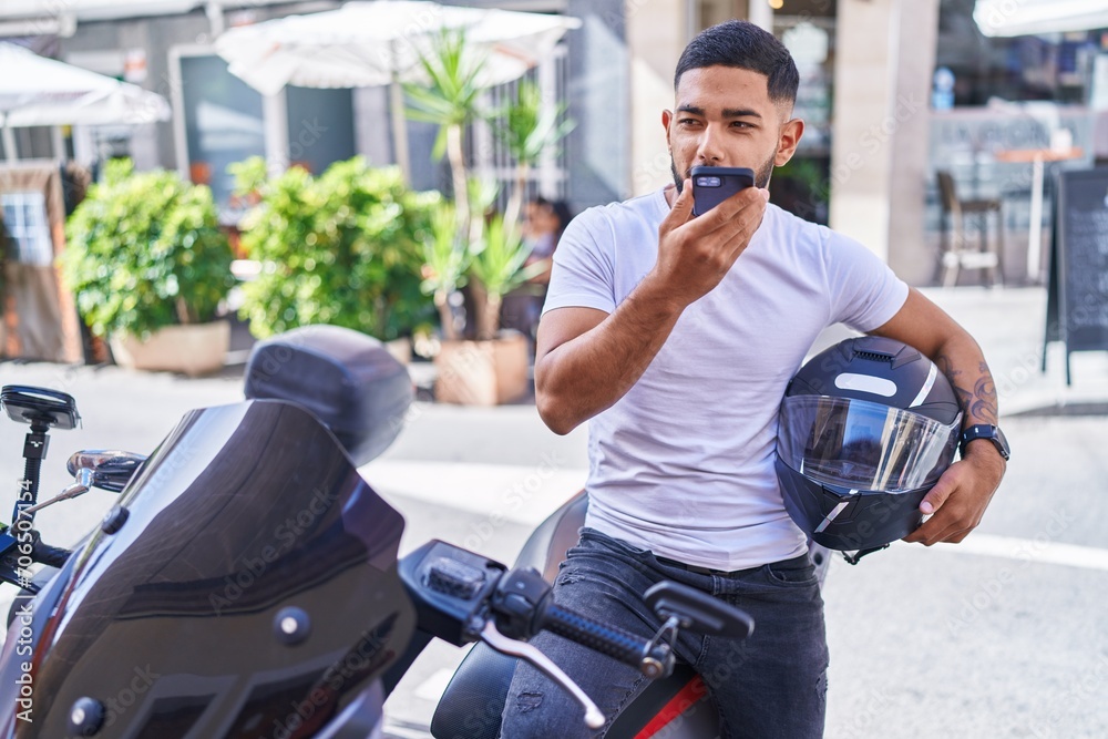Young latin man talking on smartphone sitting on motorbike at street