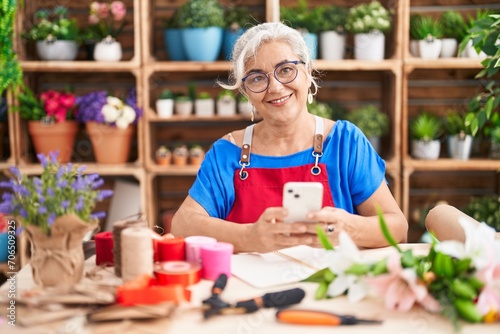 Middle age grey-haired woman florist smiling confident using smartphone at florist