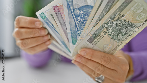 Obraz na plátne A mature woman counts various polish zloty banknotes in a bright office setting
