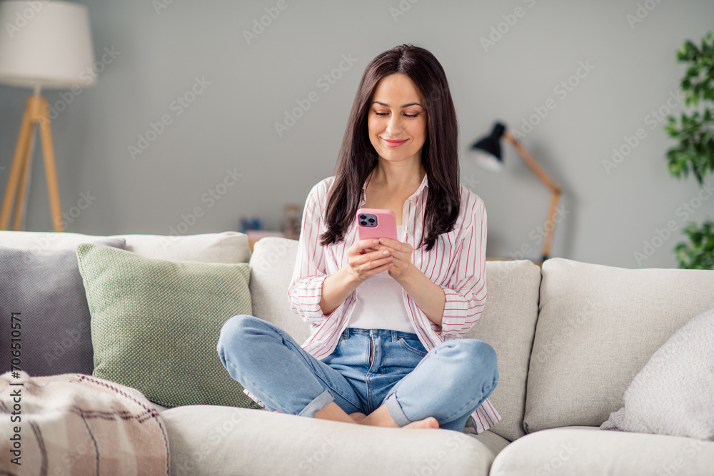 Full size portrait of positive pretty girl sit barefoot sofa use smart phone chatting communicate spend pastime apartment inside