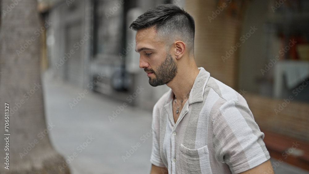 Young hispanic man sitting on bench with serious expression at street Young hispanic man sitting on bench with serious expression at street