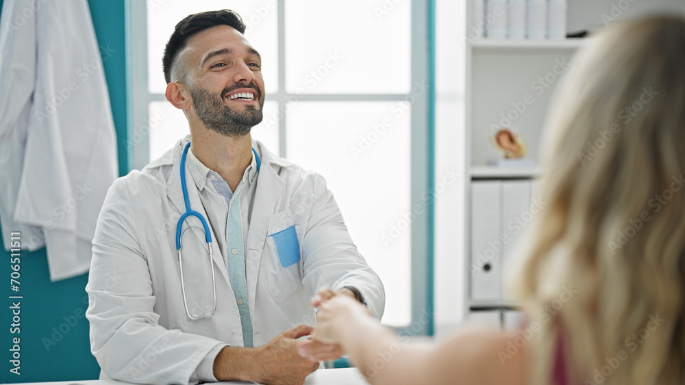 Young hispanic man doctor shaking hands with patient at the clinic