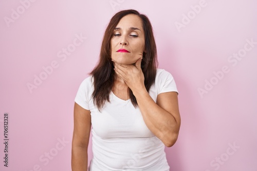 Middle age brunette woman standing over pink background touching painful neck, sore throat for flu, clod and infection