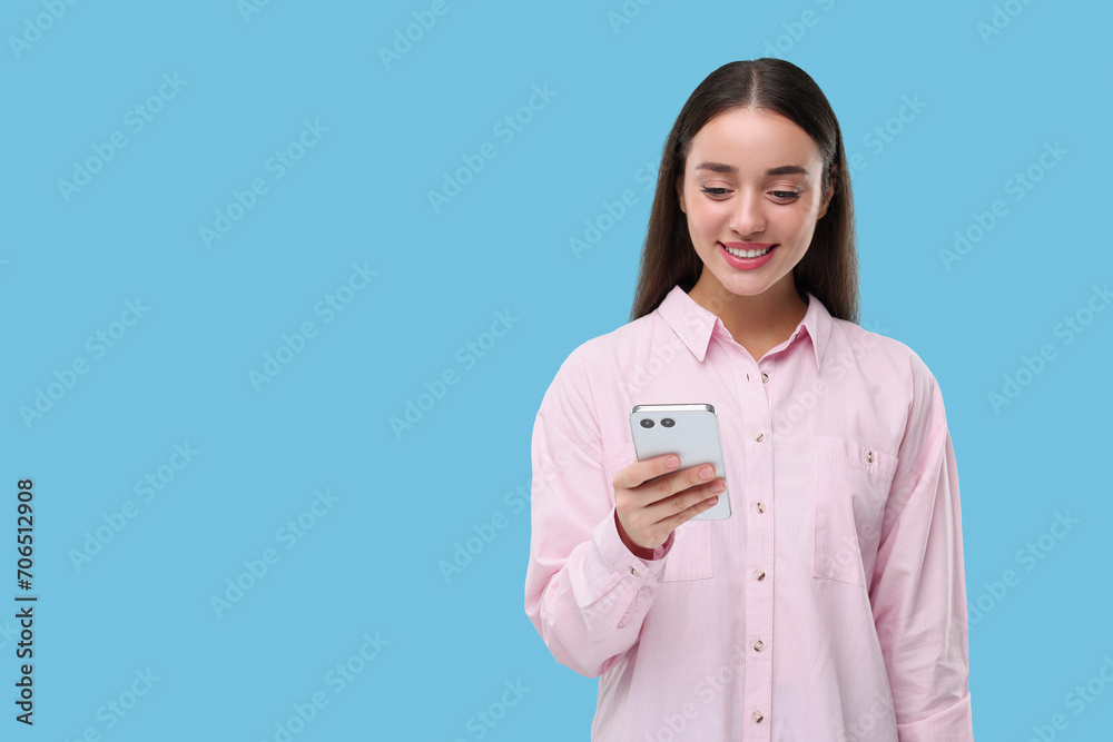 Happy woman sending message via smartphone on light blue background, space for text Happy woman sending message via smartphone on light blue background, space for text