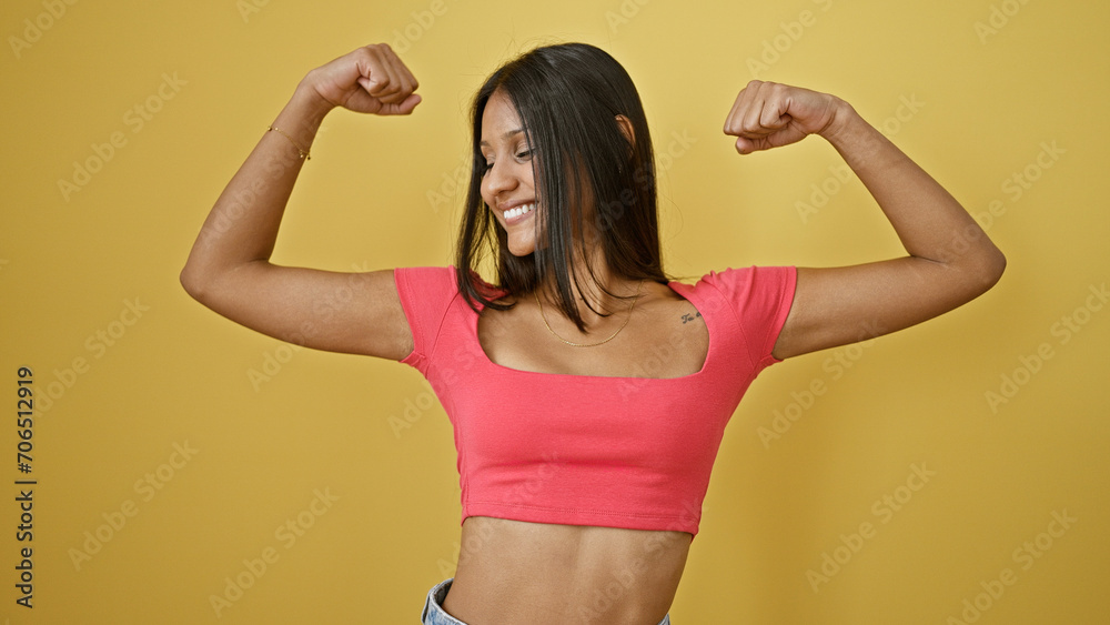 Young latin woman smiling confident doing strong gesture with arms over isolated yellow background Young latin woman smiling confident doing strong gesture with arms over isolated yellow background