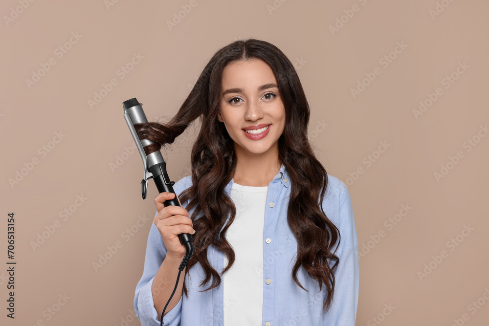 Happy woman using curling hair iron on beige background Happy woman using curling hair iron on beige background