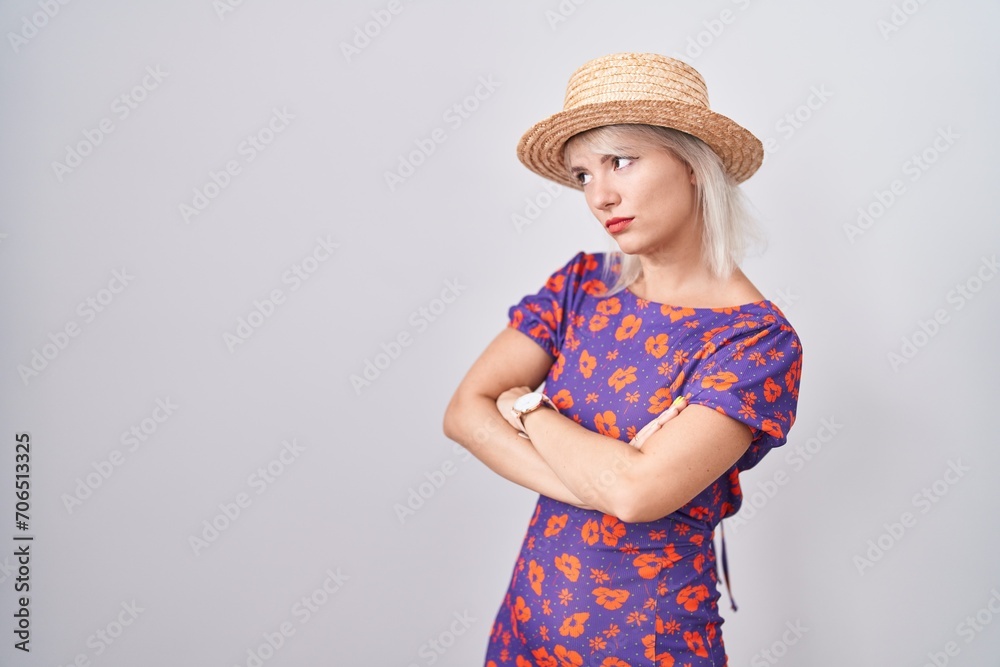 Young caucasian woman wearing flowers dress and summer hat looking to the side with arms crossed convinced and confident Young caucasian woman wearing flowers dress and summer hat looking to the side with arms crossed convinced and confident