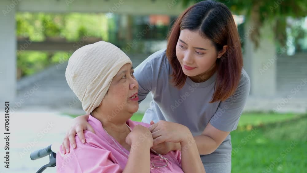 Asian careful caregiver or nurse and woman with cancer is sitting in a wheelchair. in the garden. Concept of happy retirement with care from a caregiver and Savings and senior health insurance. Asian careful caregiver or nurse and woman with cancer is sitting in a wheelchair. in the garden. Concept of happy retirement with care from a caregiver and Savings and senior health insurance.