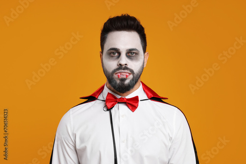 Man in scary vampire costume with fangs on orange background. Halloween celebration