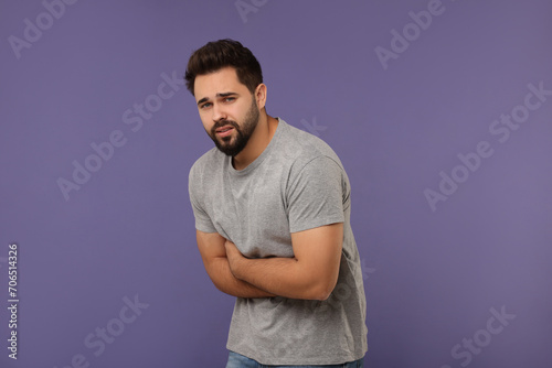 Young man suffering from stomach pain on purple background © New Africa