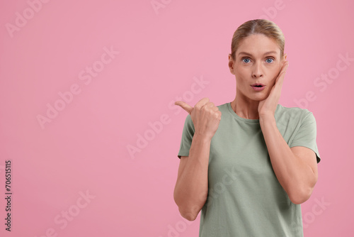 Special promotion. Surprised woman pointing at something on pink background. Space for text